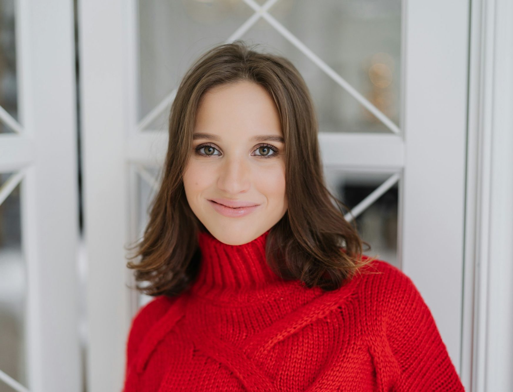 Headshot of charming woman with dark hair, wears knitted sweater, looks directly at camera